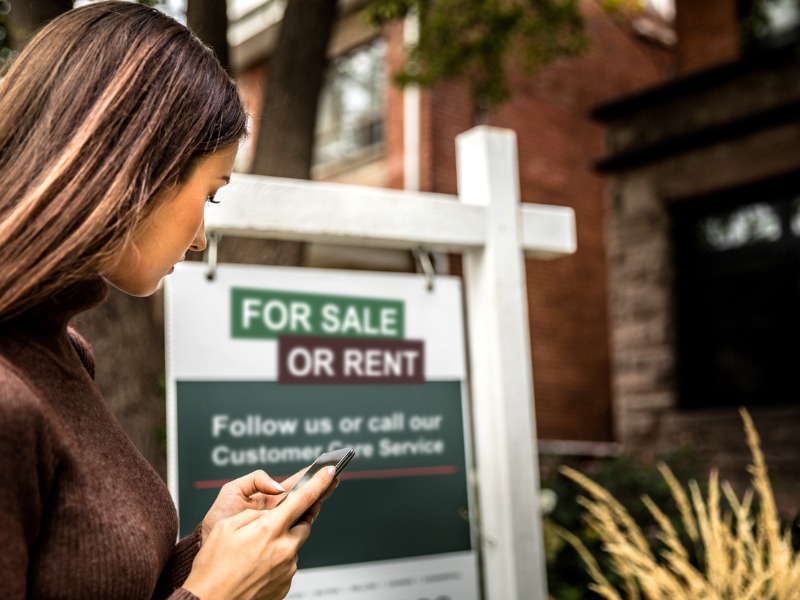 Woman photographing a real estate sign for a nice house for sale in downtown.