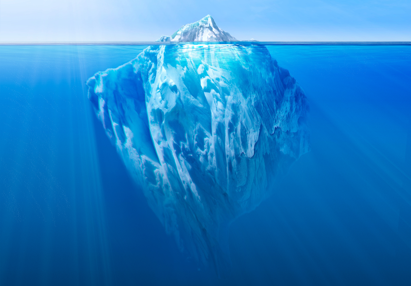 Massive iceberg floating in the ocean, with a small visible tip above water and a vast submerged section beneath. alternate text for this image