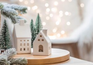 Un bouquet de sapins, un plaid dans un panier en osier et des maisons blanches scandinaves sur une table en bois à l’intérieur du salon. Un concept cosy de décoration festive pour la maison
