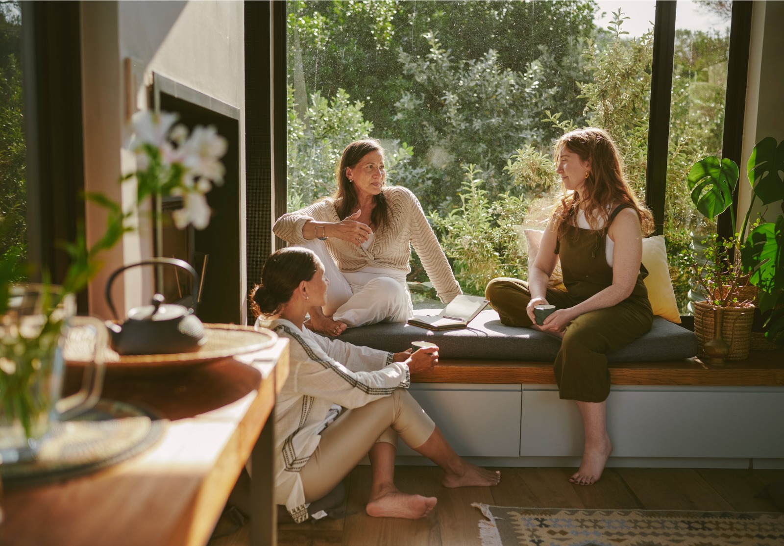 Des amies souriantes discutant ensemble près d’une fenêtre lors d’une retraite de bien-être.