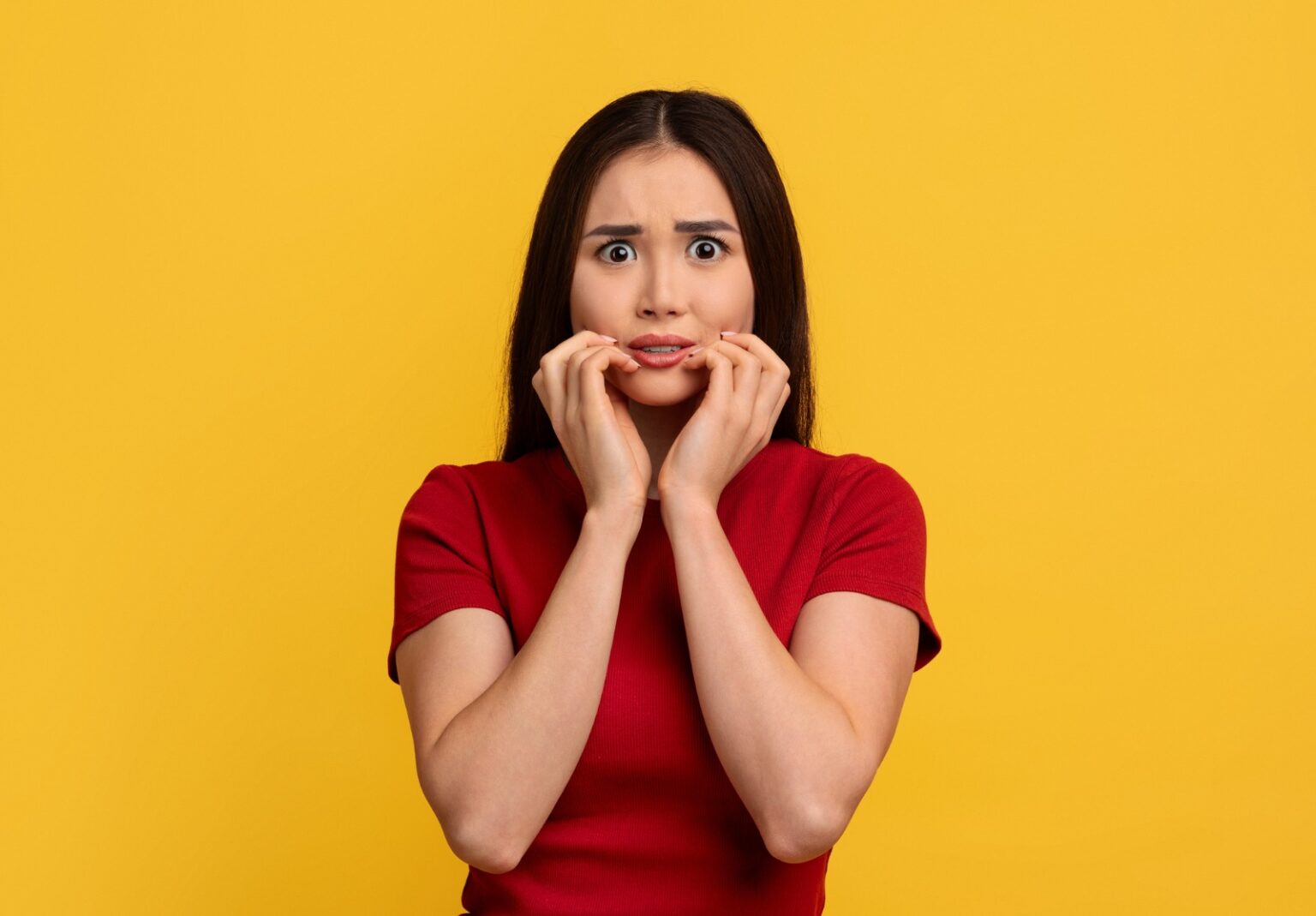Jeune femme asiatique effrayée touchant son visage, fond de mur jaune.