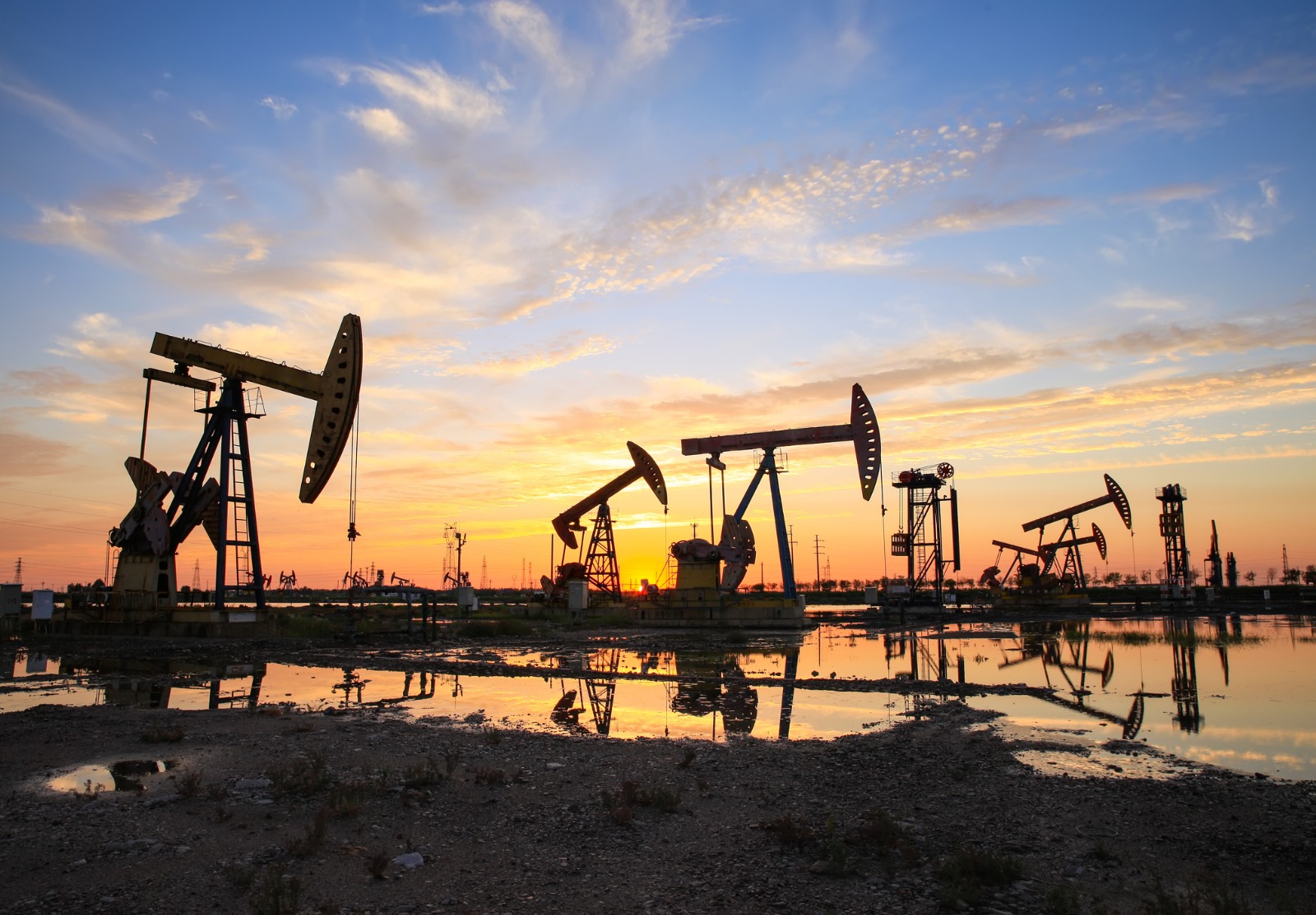 Site du champ pétrolifère, le soir, les pompes à huile fonctionnent, La pompe à huile et le magnifique coucher de soleil se reflètent dans l’eau.