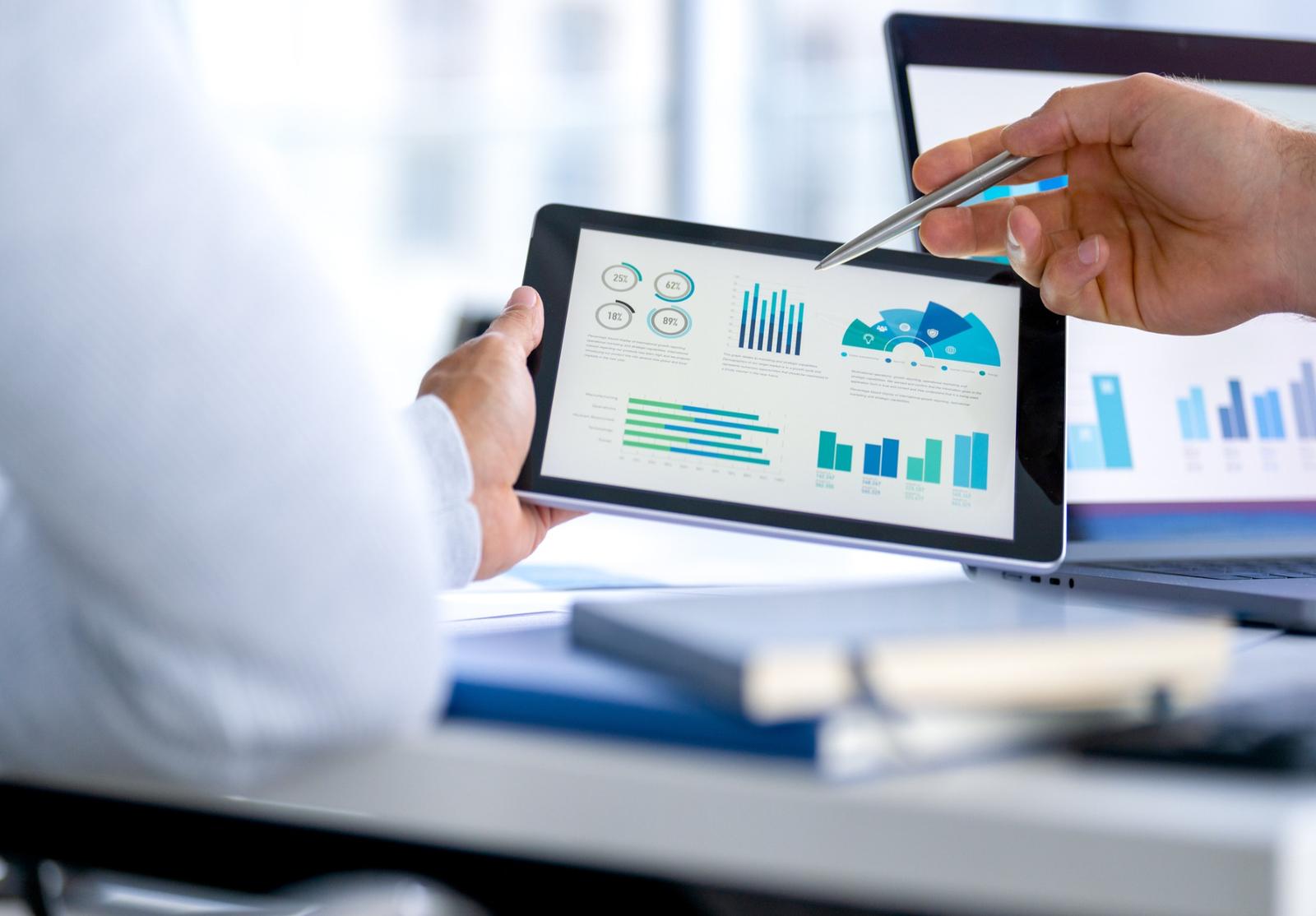Deux personnes analysent des graphiques et diagrammes présentés sur une tablette, en réunion de travail.