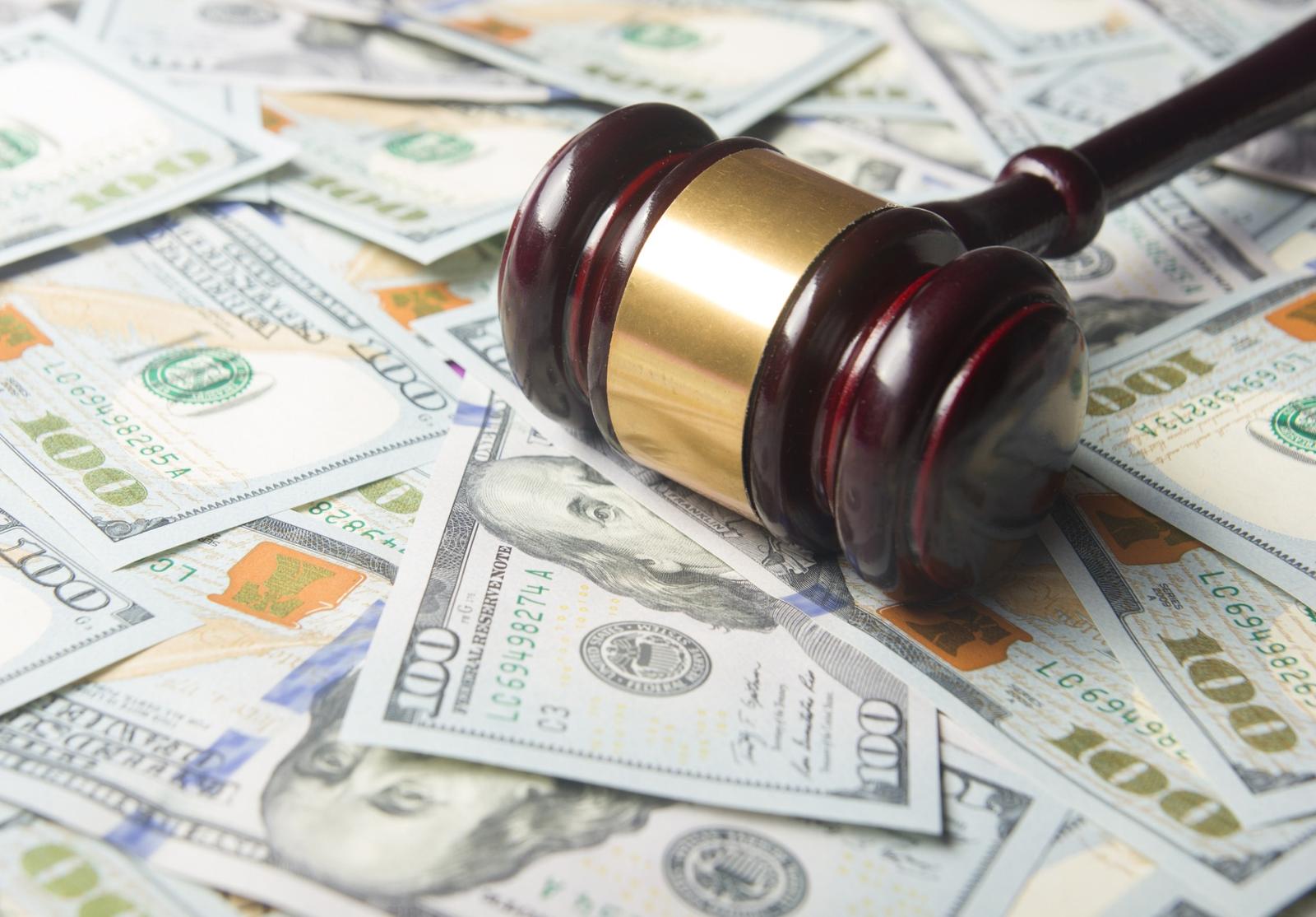 Marteau de juge posé sur une liasse de billets de 100 dollars, symbolisant le lien entre argent et justice.