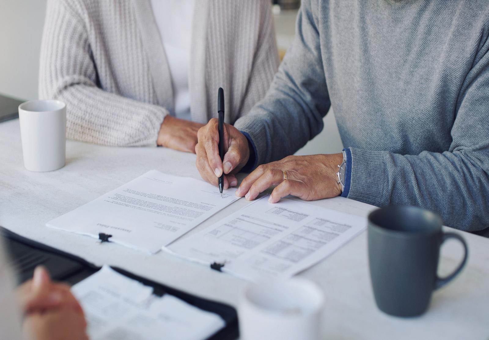 Personnes âgées signant des documents financiers ou juridiques à la maison.