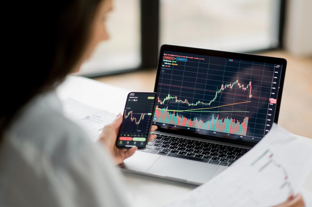 Femme analysant des graphiques boursiers sur un ordinateur portable et un smartphone. Concept d’investissement en ligne et de suivi des marchés financiers en temps réel.