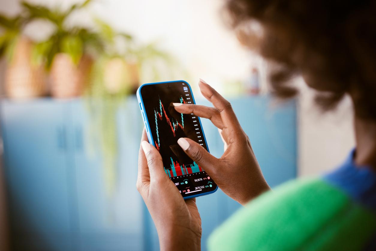 Main d’une femme utilisant une application mobile de trading affichant un graphique boursier coloré. Illustration de la finance numérique et de l’accessibilité des investissements sur mobile.
