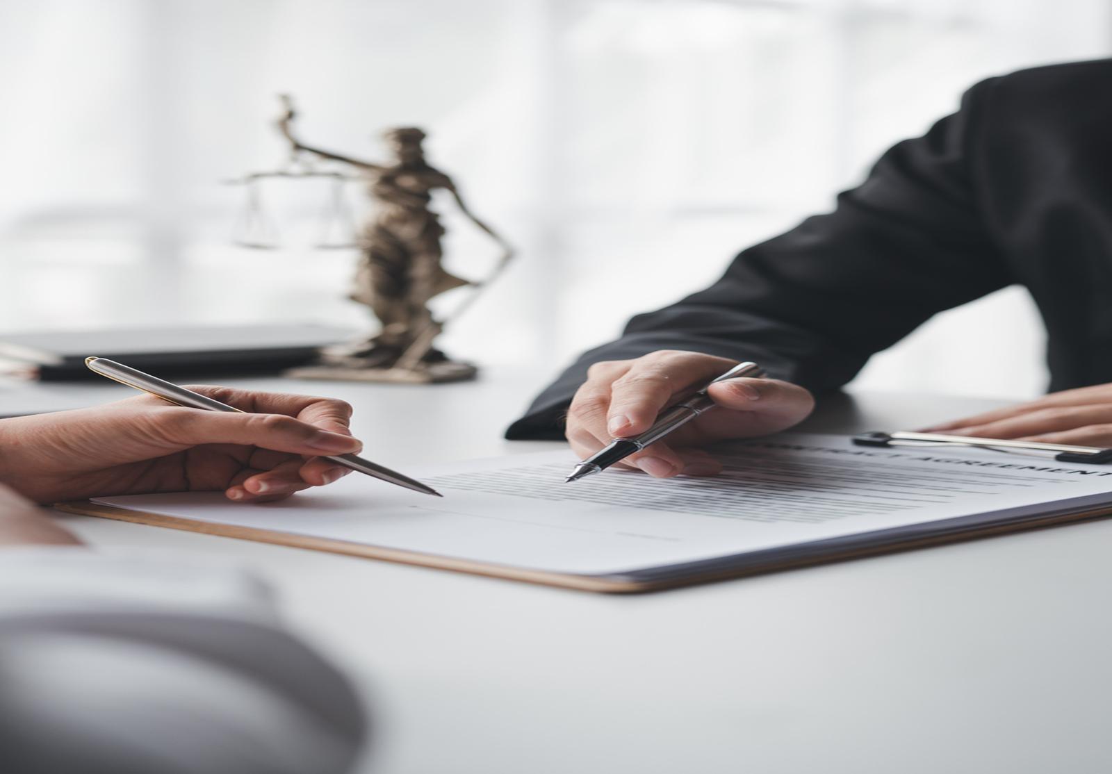 Signature d’un contrat juridique, avec une statuette de la Justice en arrière-plan.