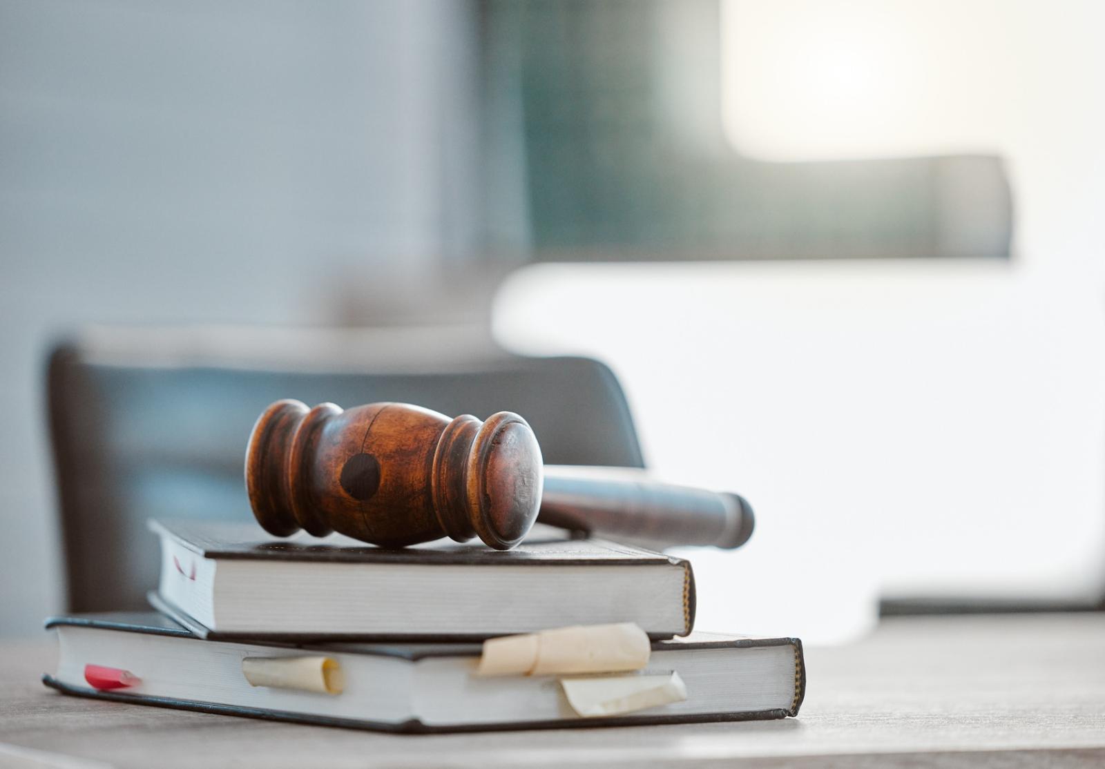 Marteau de juge en bois posé sur une pile de livres, dans un décor lumineux et sobre, évoquant le droit et l’autorité.