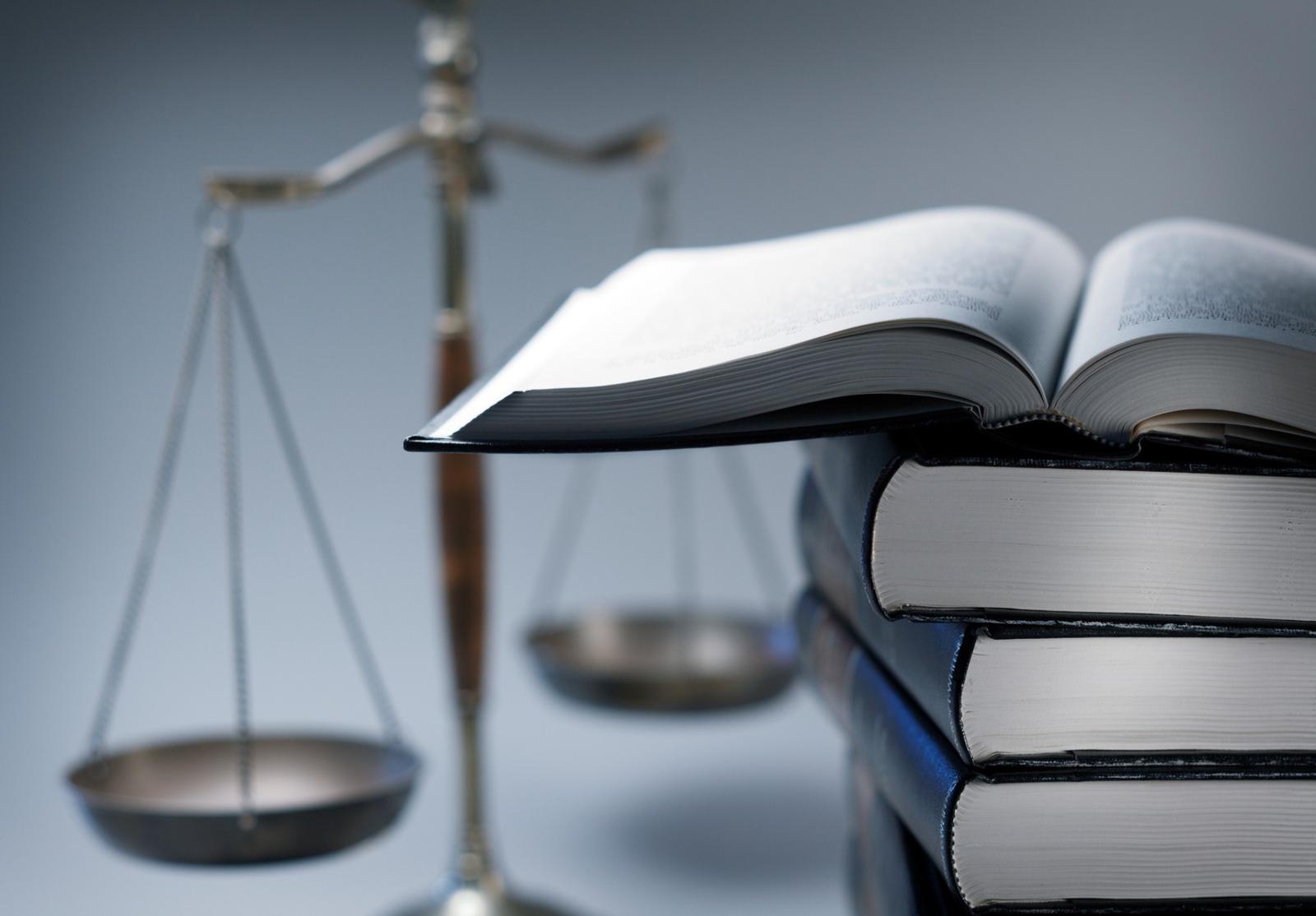 Pile de livres de droit avec une balance en arrière-plan, symbole de la justice et du savoir juridique.