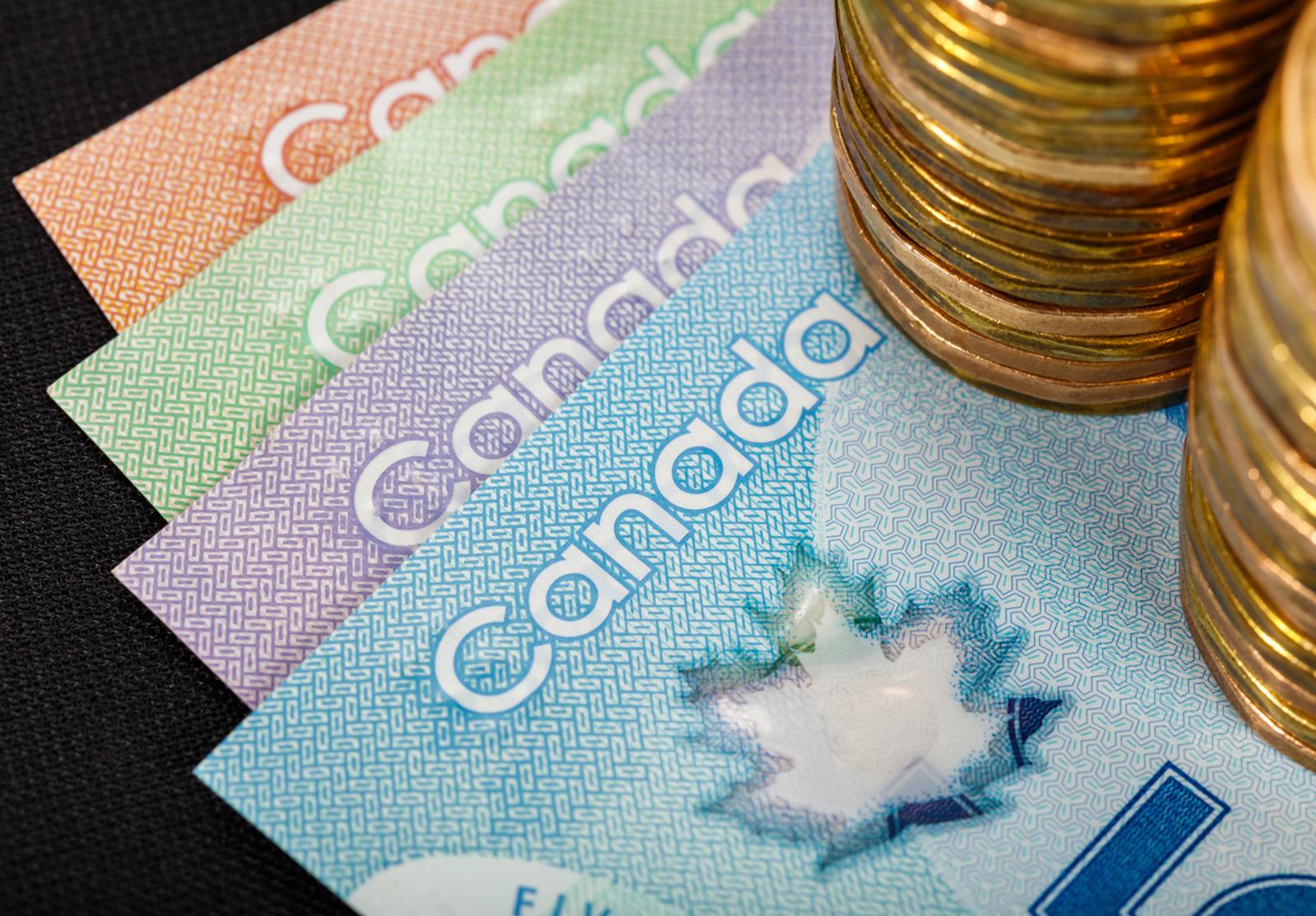 Billets canadiens colorés partiellement visibles avec des piles de pièces empilées au premier plan.