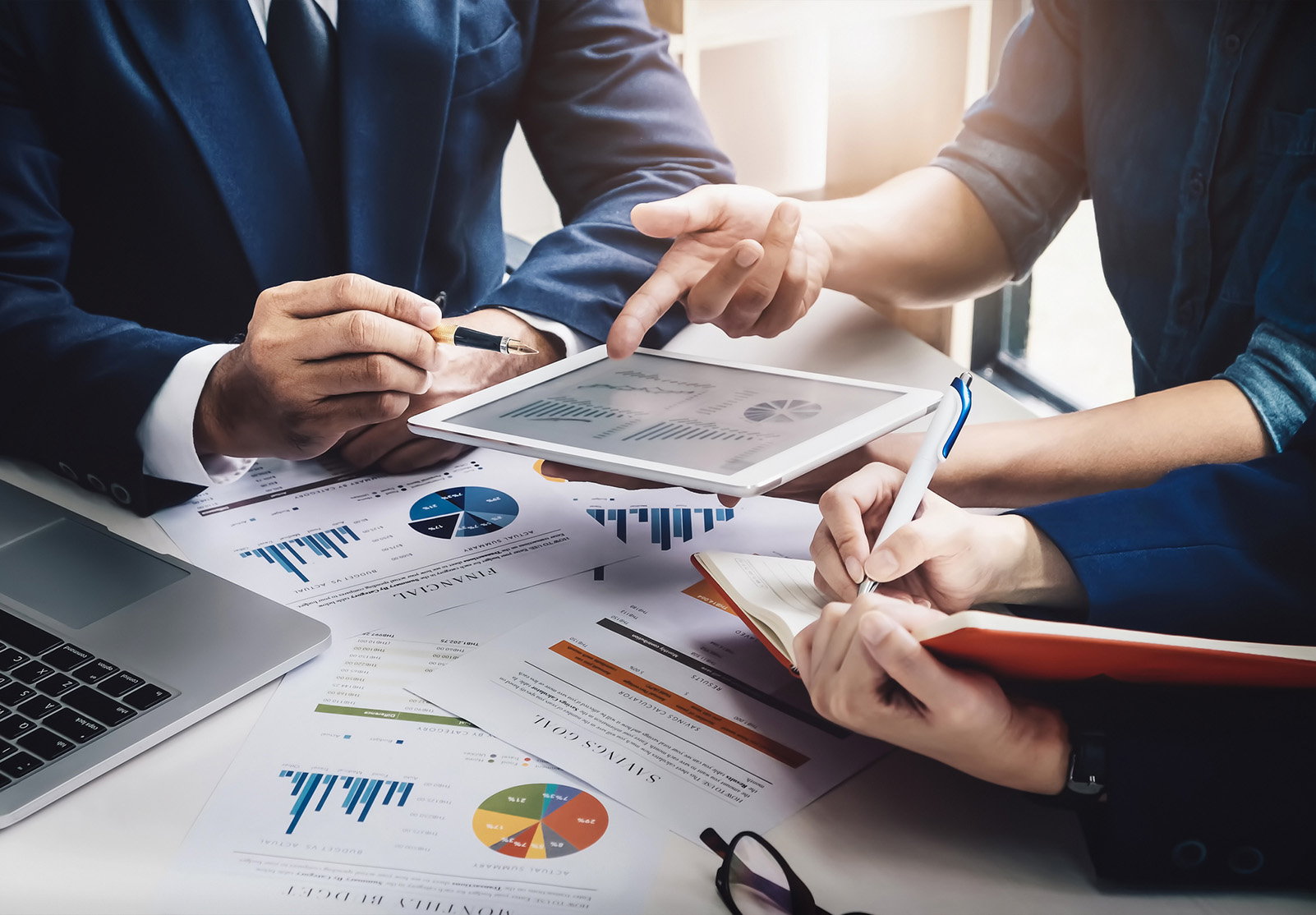 Conseillers assis à un bureau, consultant un plan marketing, utilisant une tablette et un ordinateur.